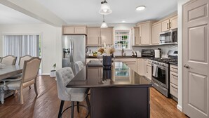 Une cuisine moderne dotée d’un îlot central, d’appareils électroménagers en acier inoxydable et de meubles de rangement en bois clair.