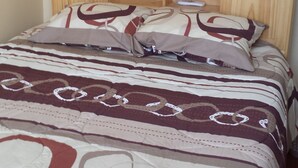 Un letto con una coperta e cuscini decorati, una testiera in legno e un comodino con un telecomando.