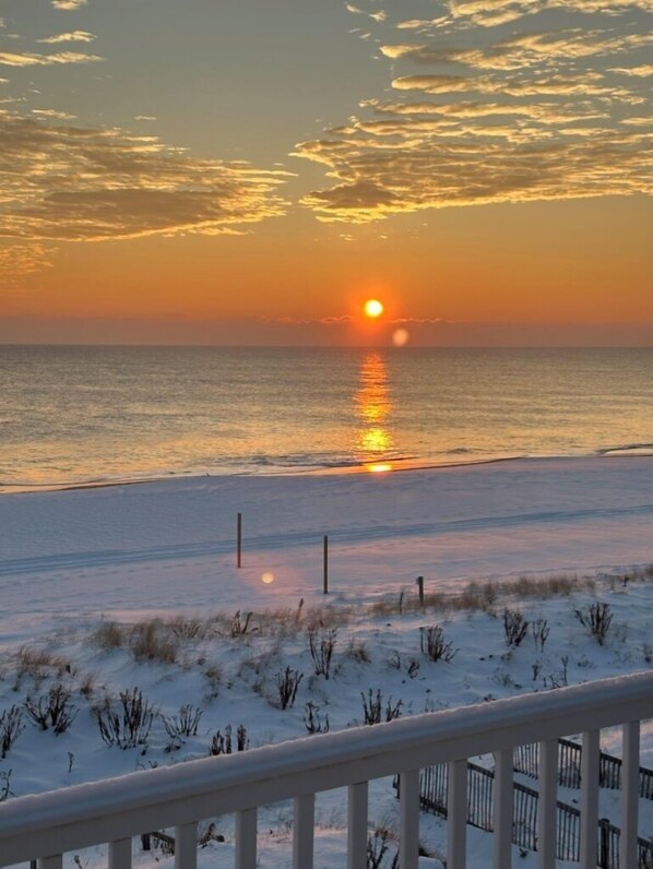 A sunset over a snowy beach with a railing in the foreground.