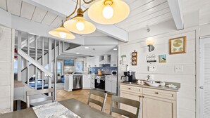 Een moderne keuken met witte kastjes, een eethoek met een houten tafel, en een trap naar een hoger niveau.