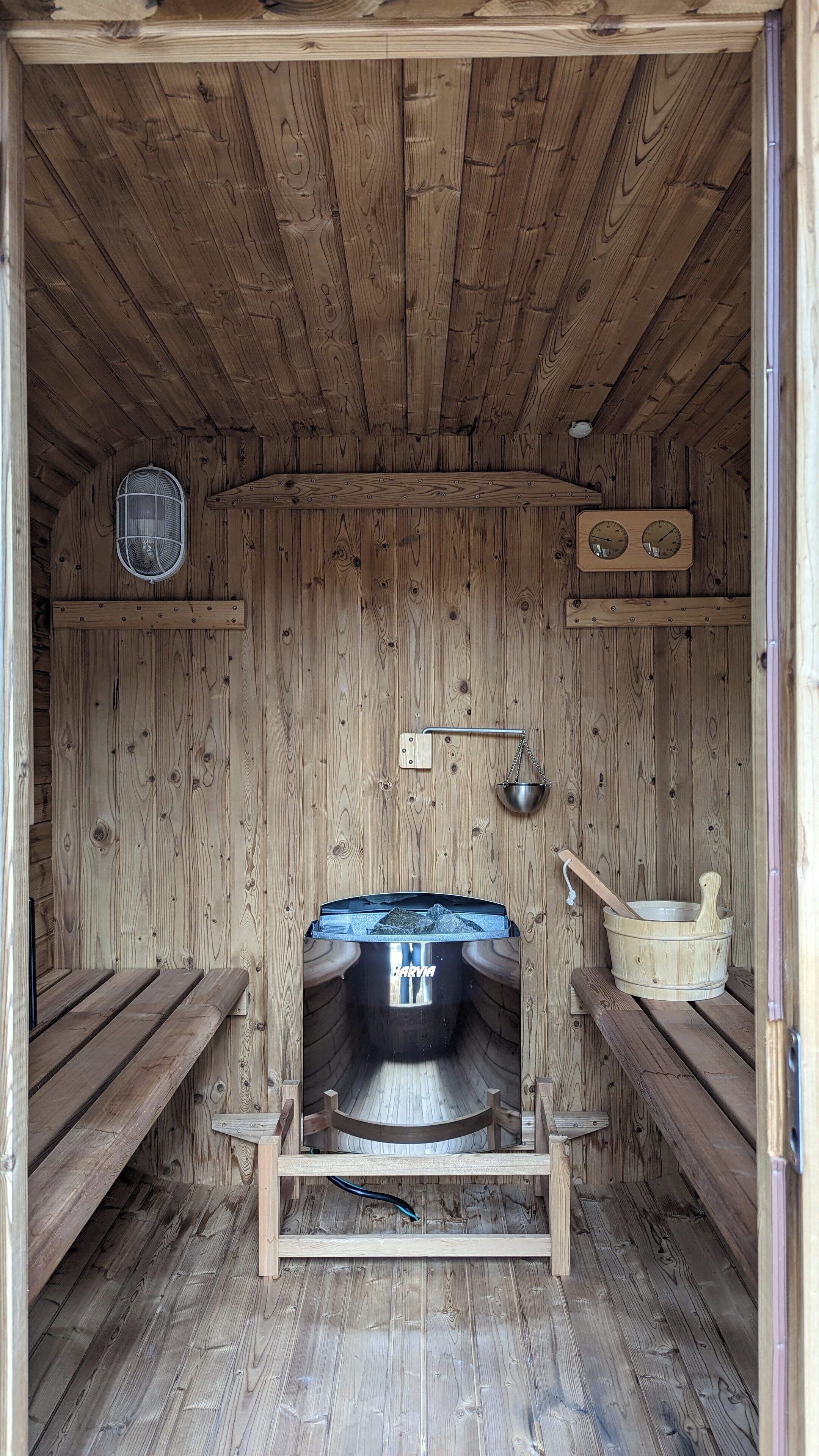 A wooden sauna with benches, a hot tub, and a wooden bucket.