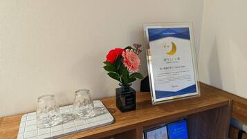 A wooden reception desk with a framed certification certificate, a small vase with flowers, and two empty glasses on a white mat.