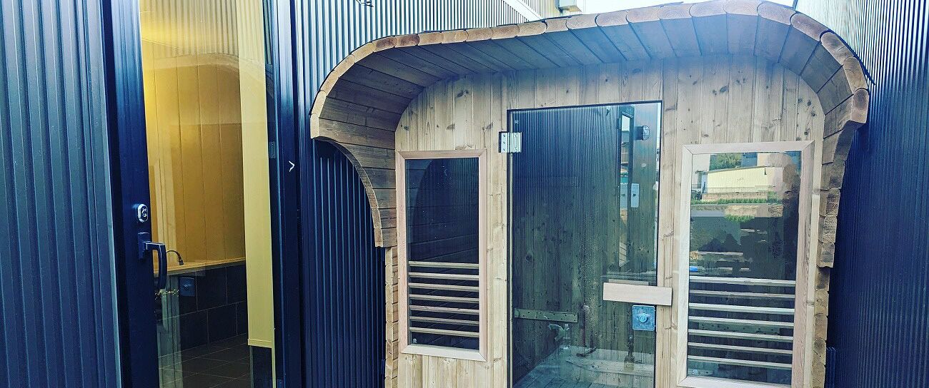 Una estructura de madera con dos puertas de vidrio, barandal metálico y una puerta de metal con manija.