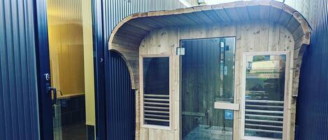 Una estructura de madera con dos puertas de vidrio, barandal metálico y una puerta de metal con manija.