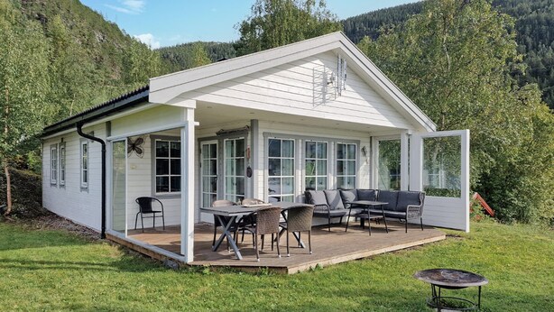 Een witte blokhut met een overdekte patio, ingericht met een tafel, stoelen en een bank.