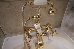 Un bagno con rubinetteria dorata per doccia e vasca, un erogatore di sapone bianco e un soffione con tubo flessibile.