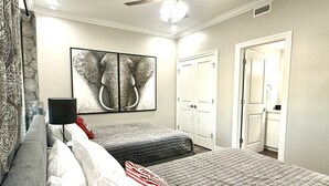 Ein Schlafzimmer mit zwei Betten, einem Deckenventilator, einem großen Elefantenbild und einer Tür zu einem Badezimmer.