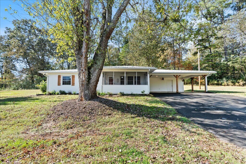 A single-story house with a front porch, a large tree in front, and a driveway.