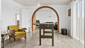 A spacious room with a wooden floor, a yellow armchair, a table, and a foosball table. - 4 bedroom nice home in Harboøre (Harboøre)