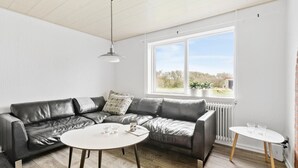 A modern living room with a leather sofa, a round coffee table, and a small side table. A large window provides a view of the outdoors. - 4 bedroom nice home in Harboøre (Harboøre)