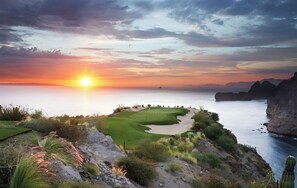 Um campo de golfe com vista para o oceano e falésias ao pôr do sol.