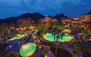 Resort com vários edifícios, palmeiras e área de piscina com elementos aquáticos.