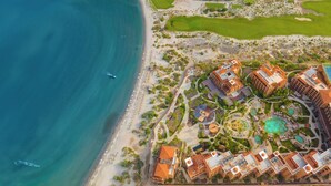 Vista aérea de un resort costero con varias construcciones, una playa y un campo de golf.