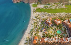 Vista aérea de um resort à beira-mar, com vários edifícios, uma praia e um campo de golfe.