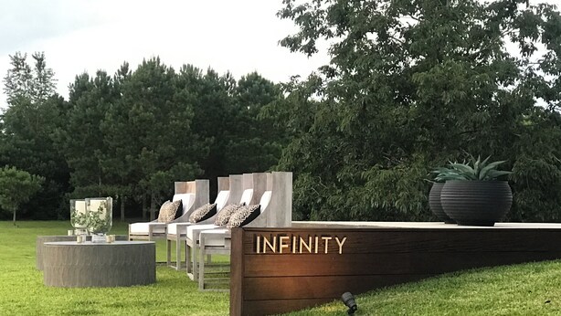 Un espace verdoyant avec des chaises longues et un banc en bois sur lequel est inscrit le mot « INFINITY ».