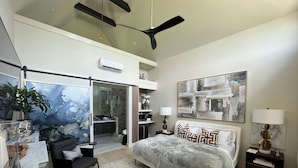 Une chambre moderne avec un grand lit, un bureau, une chaise, un ventilateur de plafond et une grande fenêtre.