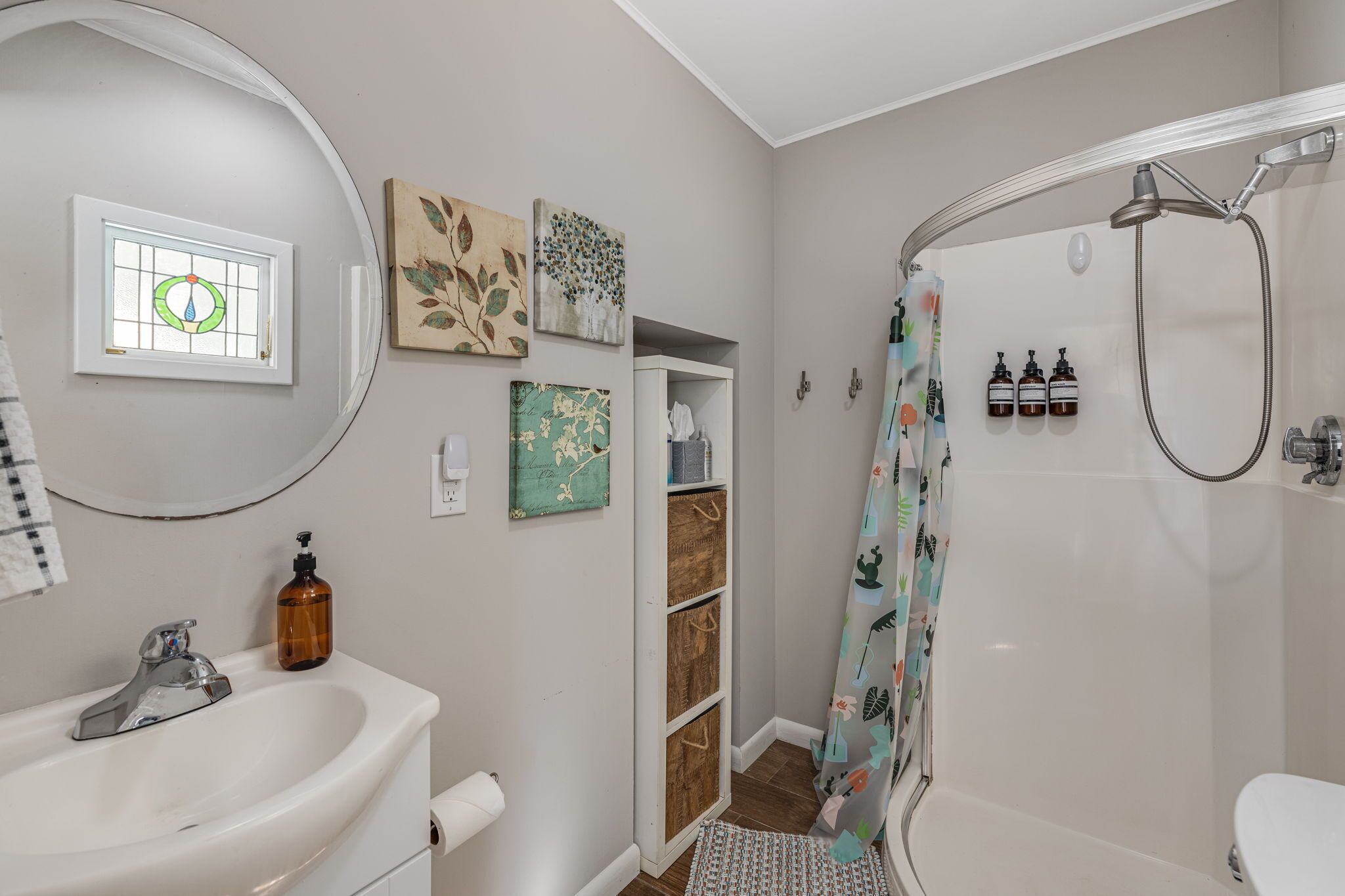 A bathroom with a sink, mirror, shower, and decorative wall art.