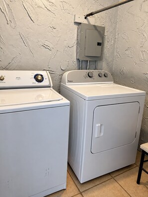 A laundry room with a front-loading washer and dryer, a utility meter, and a wall-mounted electrical box. - Entire Cozy House  Near UTEP (El Paso)
