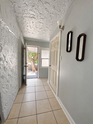 A hallway with a white textured ceiling, a white door, and two wall-mounted mirrors. - Entire Cozy House  Near UTEP (El Paso)
