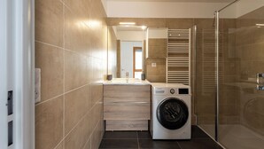 Un baño moderno con lavadora incorporada, cabina de ducha de cristal y tocador de madera.