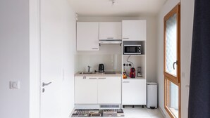 Una cocina compacta con armarios blancos, un microondas, un hervidor y una licuadora sobre la encimera.
