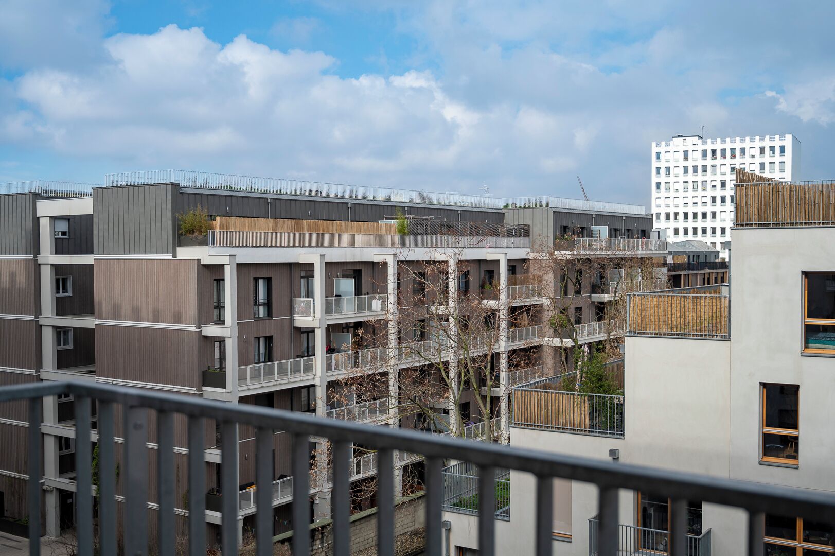 Un immeuble résidentiel à plusieurs étages, doté de balcons et d’une architecture moderne, offrant une vue sur un bâtiment plus haut en arrière-plan.