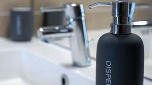 Un lavamanos con una botella dispensadora negra etiquetada como "DISPENSER" y una llave moderna.