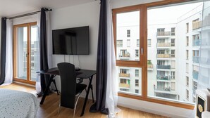 Una habitación de hotel moderna con un ventanal grande, un escritorio con silla y un televisor de pantalla plana.