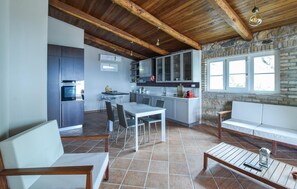 A modern kitchen with a dining area, stone wall, and large windows. - Nice home in Satriano (Satriano)