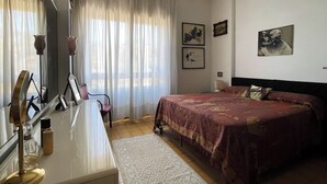 A bedroom with a bed, a desk with a mirror, a chair, and a window with curtains. - di Alfredo (Roma)