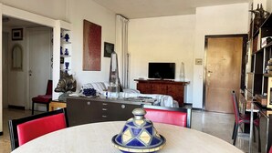 A dining area with a round table, chairs, a decorative blue and gold centerpiece, a television on a wooden cabinet, and a bookshelf with various items. - di Alfredo (Roma)