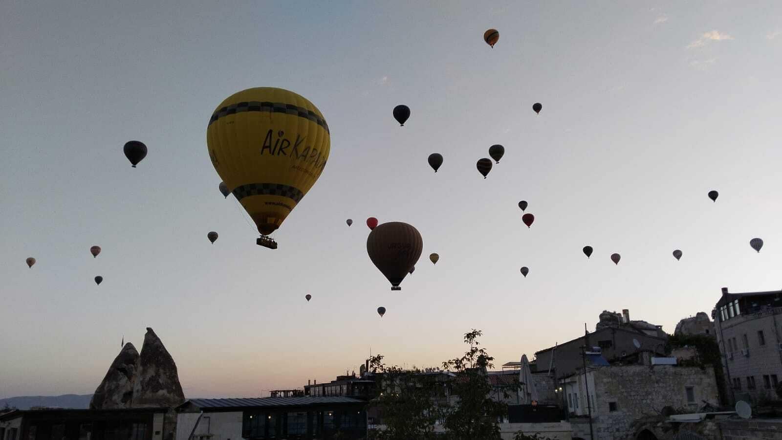 A cityscape with several hot air balloons, including one labeled "Air Kapla," against a clear sky.
