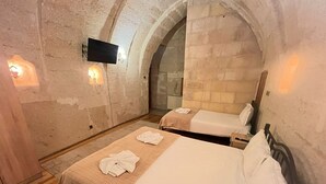 Une chambre avec deux lits, un téléviseur à écran plat fixé au mur et des murs en pierre.