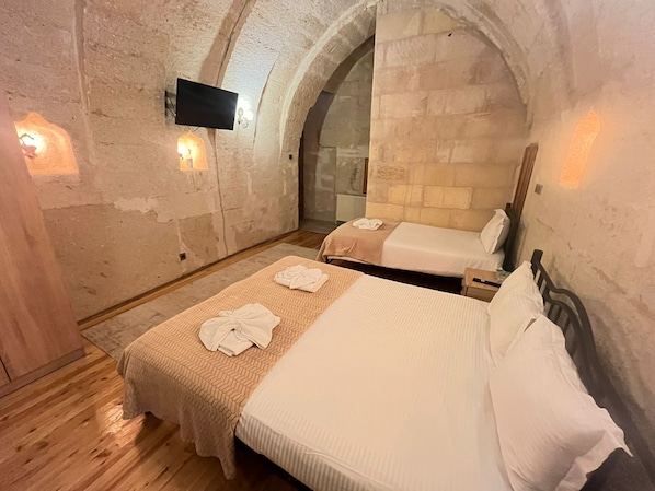 A room with two beds, a flat-screen TV mounted on the wall, and stone walls. - Mustafa Bey Konağı (Nevsehir)