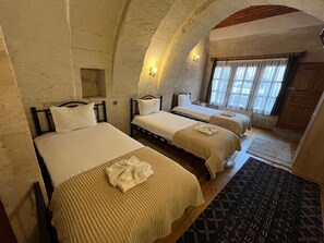 A room with three beds, a wooden floor, a stone wall, and a window with curtains.