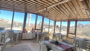 Un espace extérieur abrité, aménagé pour les repas, avec des tables et des chaises, de grandes fenêtres et une vue sur le paysage urbain.
