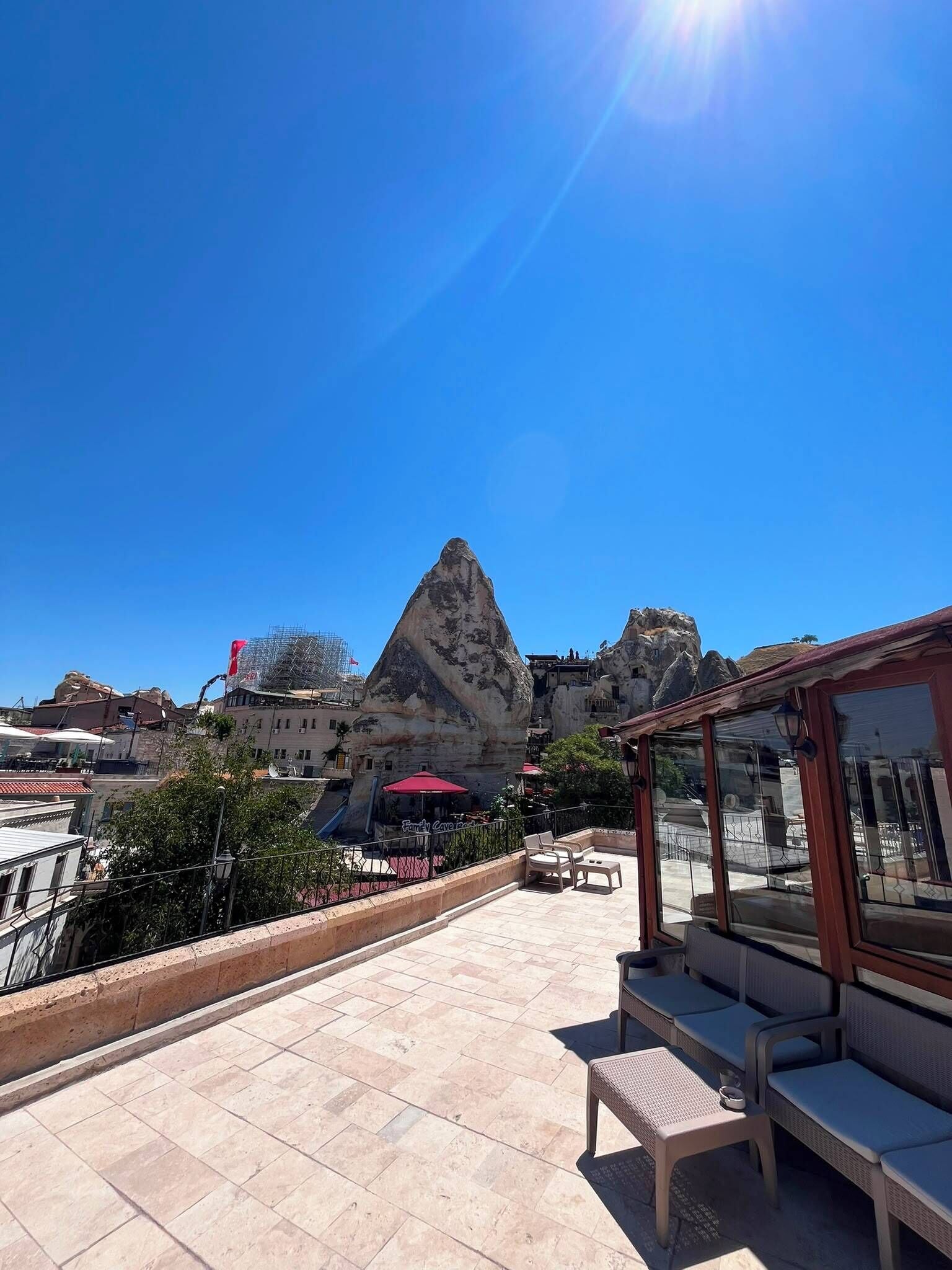 A terrace with outdoor seating, a rock formation, and buildings in the background.