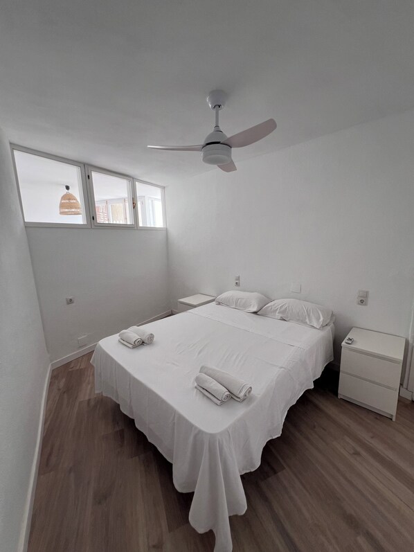 A bedroom with a bed, a nightstand, a ceiling fan, and a window.
