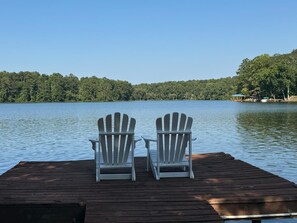 Dos sillas Adirondack en un muelle de madera con vista a un lago bordeado por un bosque.