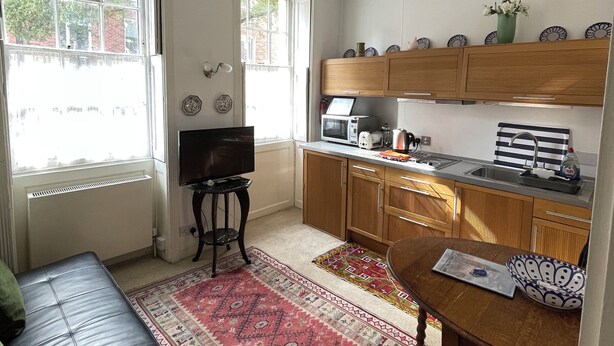 A compact kitchen with a dining area, a TV, and a window with a view of the street.