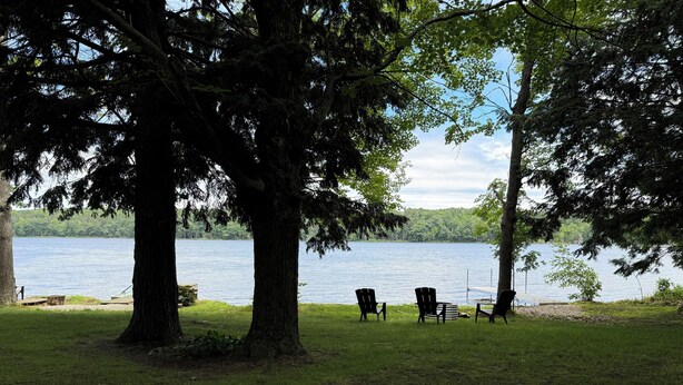 Vista sul lago con tre poltrone Adirondack rivolte verso l'acqua, immerse nel verde.