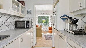 Una cocina moderna con microondas, cafetera y armarios. Se observa un comedor con una mesa y sillas.