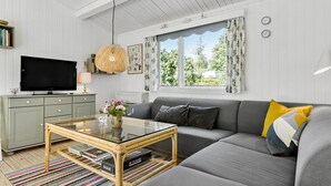 Una sala de estar moderna con un sofá gris, una mesa de centro de vidrio, un televisor y un ventanal con cortinas florales.