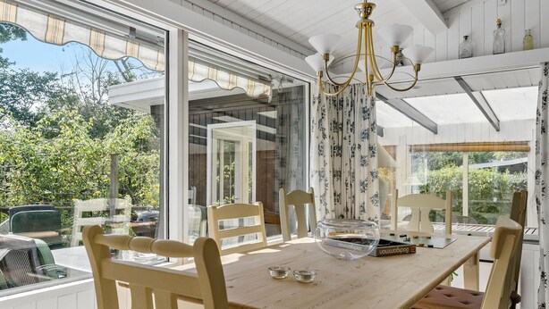 Comedor con mesa de madera, cuatro sillas, una araña y ventanas amplias con cortinas.