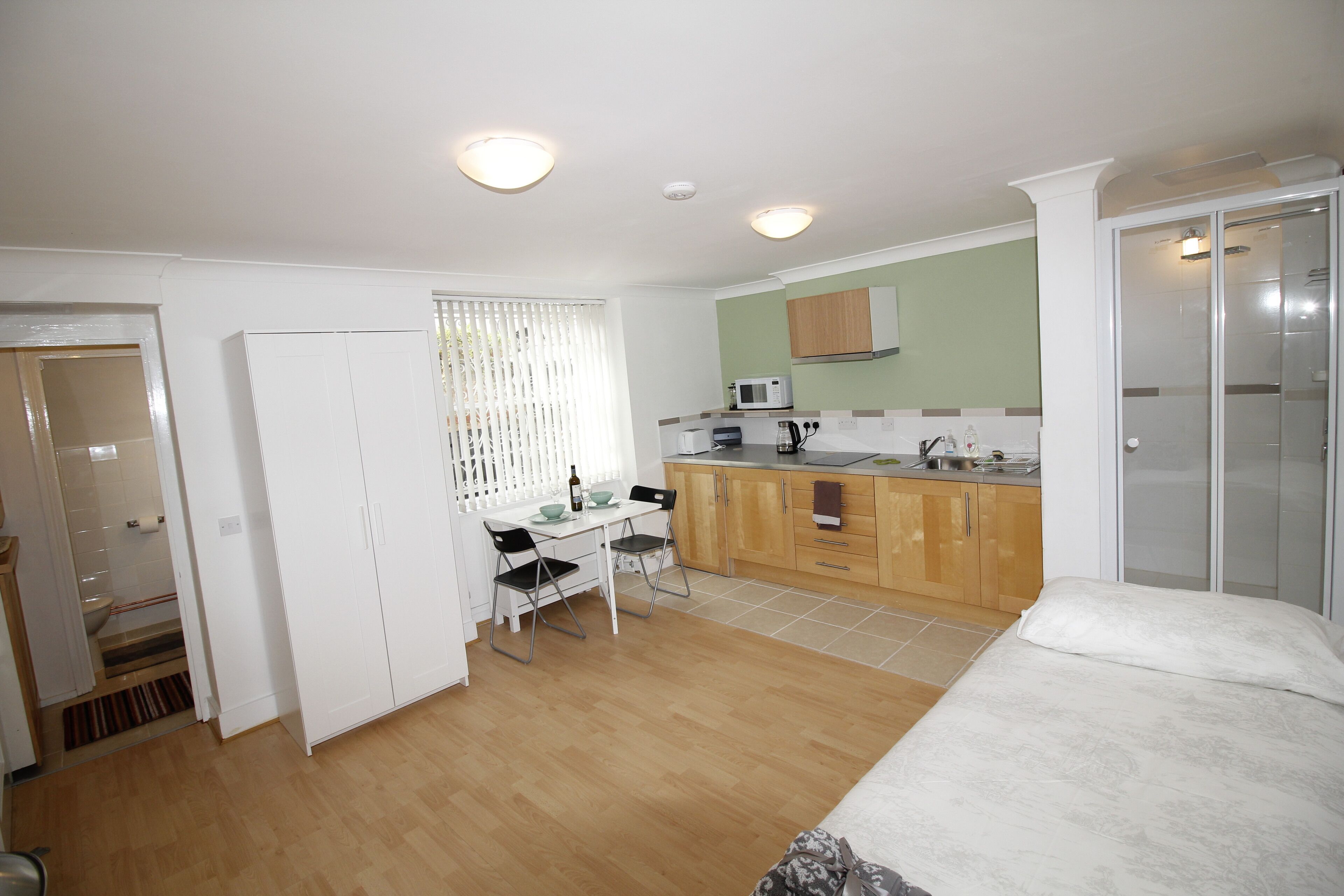Une pièce de taille modeste comprenant un lit, une petite table à manger avec des chaises, un coin cuisine et un espace douche.