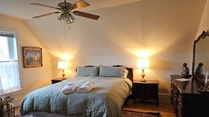A bedroom with a bed, two bedside tables with lamps, a ceiling fan, a dresser, and a mirror. - Baxter Manor Spring City (Spring City)