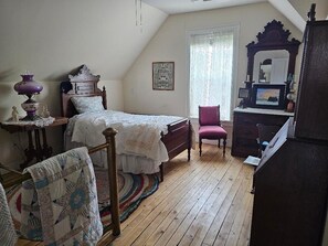 A bedroom with a wooden floor, a bed with a white bedspread, a dresser, a chair, and a mirror.