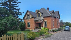 A two-story brick house with a front porch, a picket fence, and a gravel driveway. - Baxter Manor Spring City (Spring City)