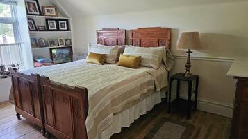 A bedroom with a wooden bed, a bedside table, a lamp, and a shelf with framed photos.