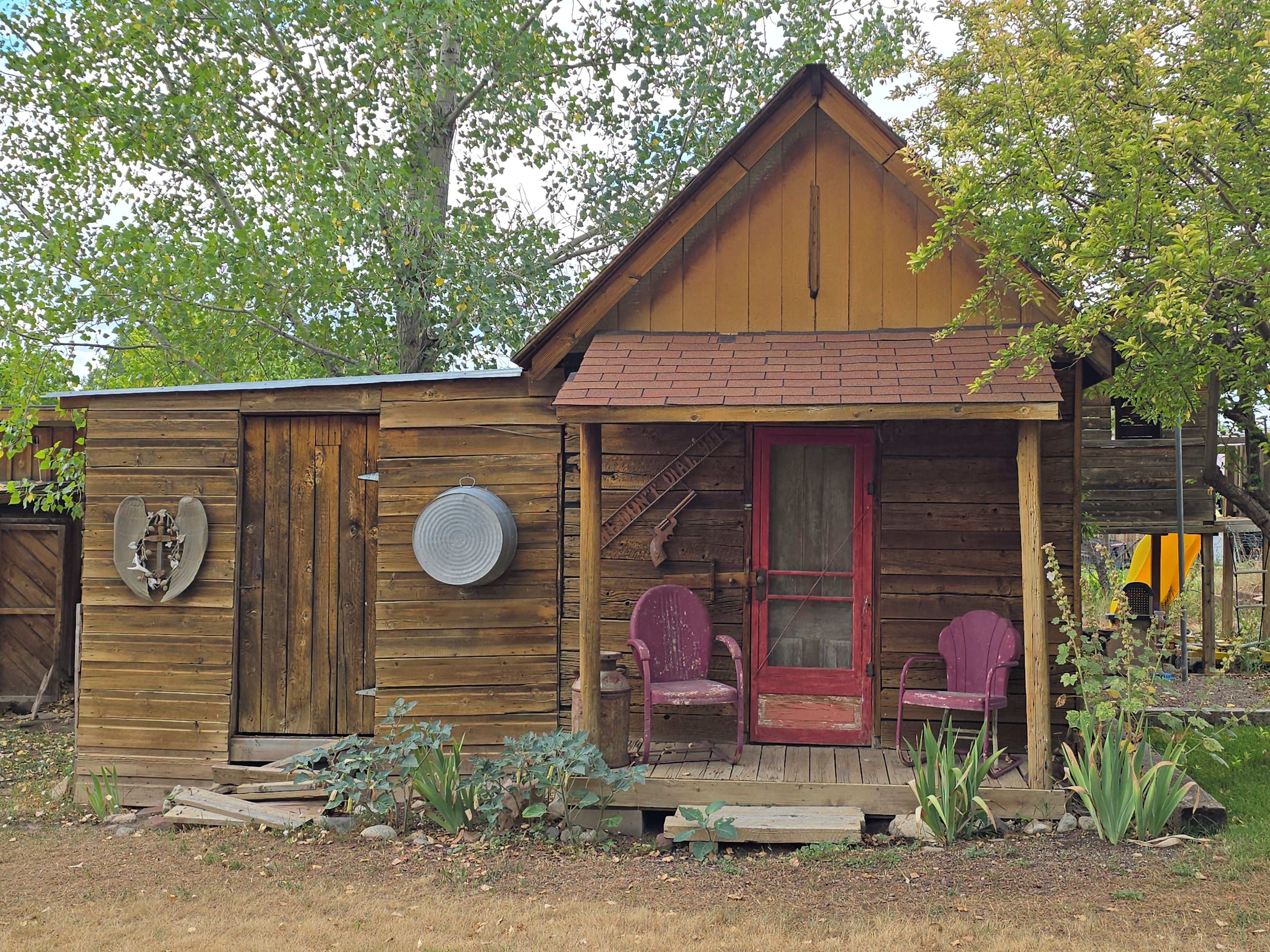 A wooden cabin with a porch, two chairs, and a small garden area.